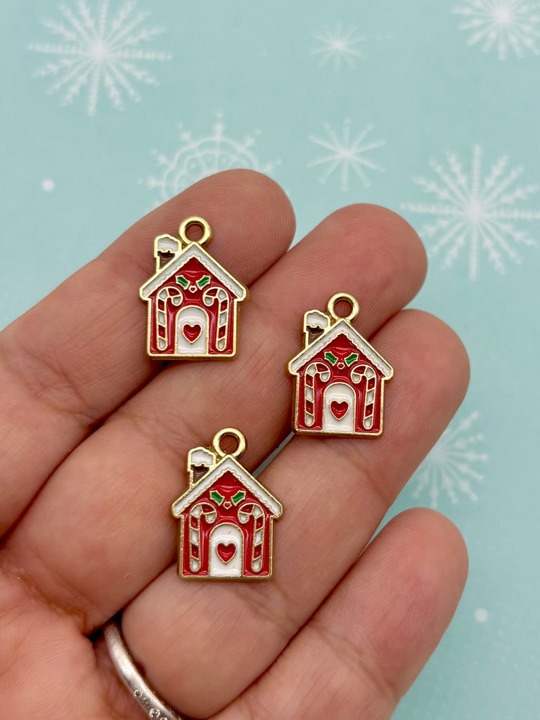 A hand holding three small, red and white house-shaped charms against a blue background with white snowflakes.