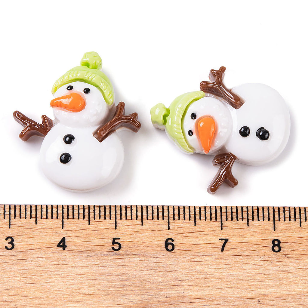 Two snowman figurines with orange noses and green hats are placed next to a ruler on a wooden surface.