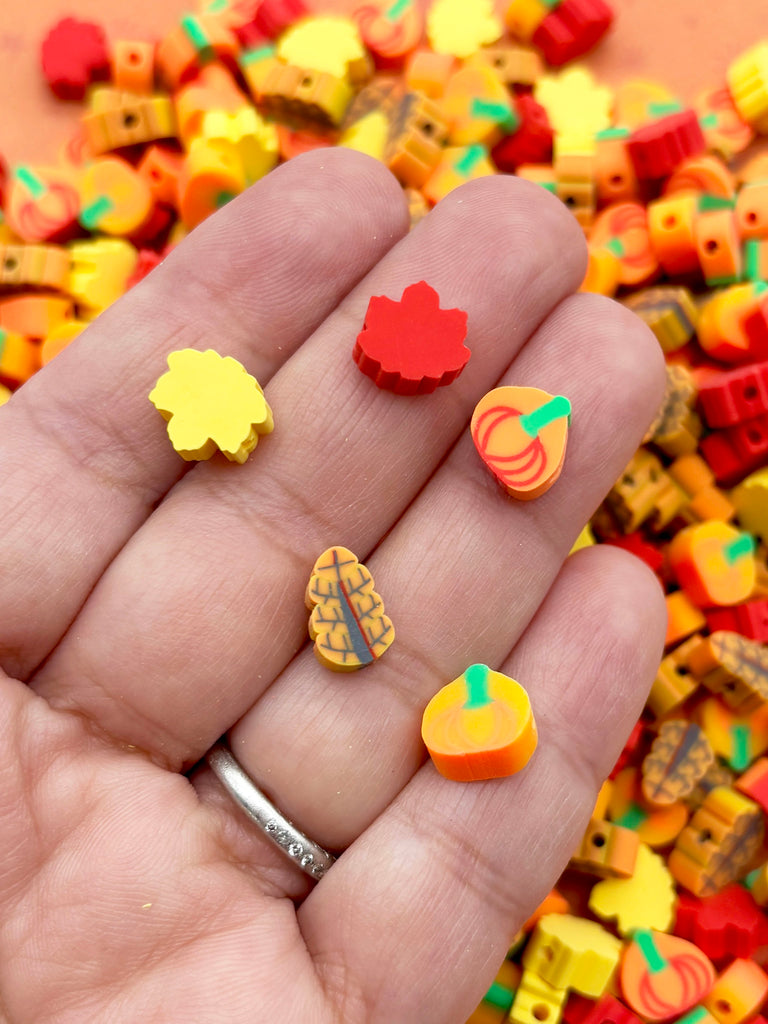 A hand holding a collection of colorful beads, including leaves, pumpkins, and other autumn-themed shapes.