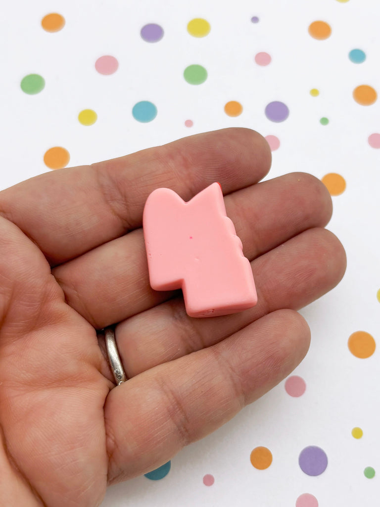 A hand holding a small, pink object against a background with colorful polka dots.