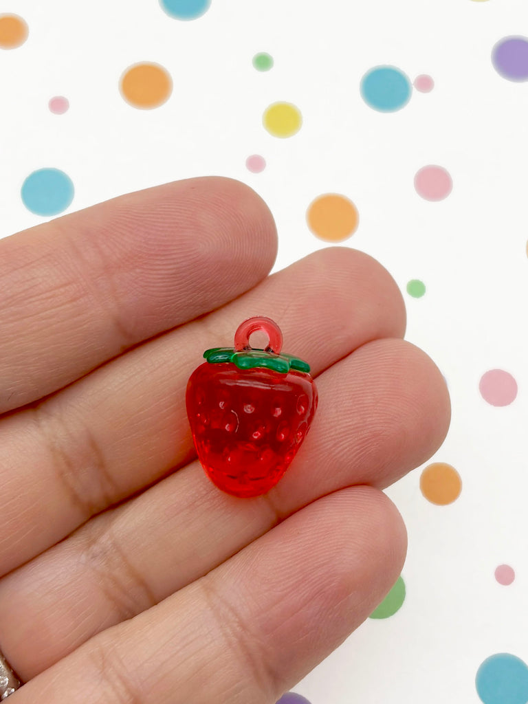 A hand holding a small, red, plastic strawberry charm against a background of colorful polka dots.