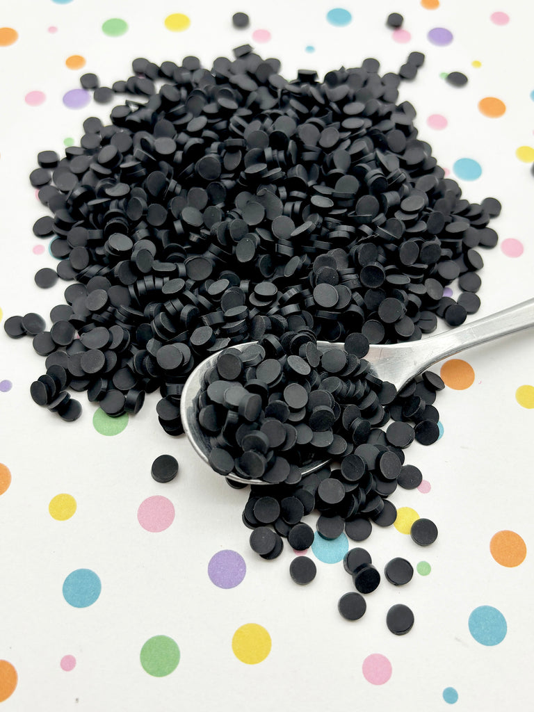 a pile of black circular objects, possibly beads or buttons, scattered on a surface with colorful polka dots. A spoon is also visible, with some of the black objects spilling out onto the spoon.