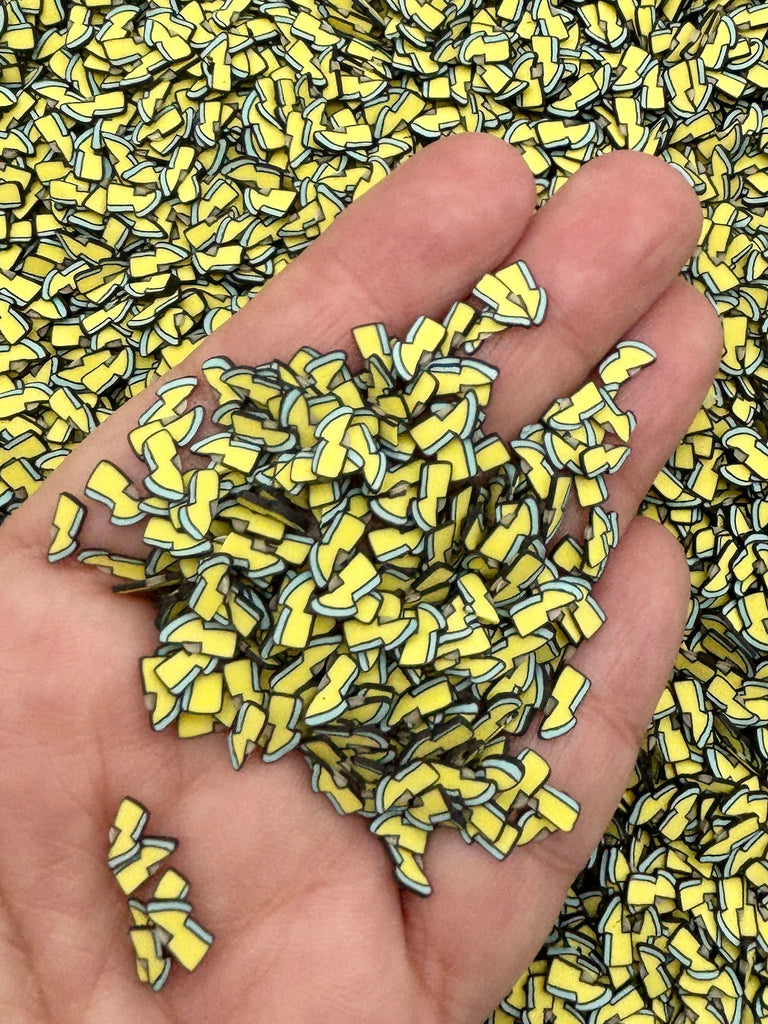 A hand is holding a pile of yellow and black objects, which appear to be small, colorful beads or sequins.