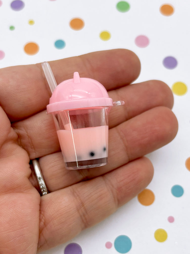 A hand holding a small pink cup with a straw, against a background with colorful polka dots.