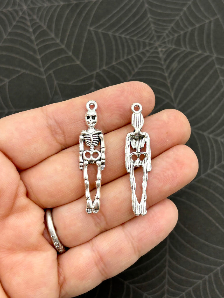 a person holding two small skeleton charms in their hand