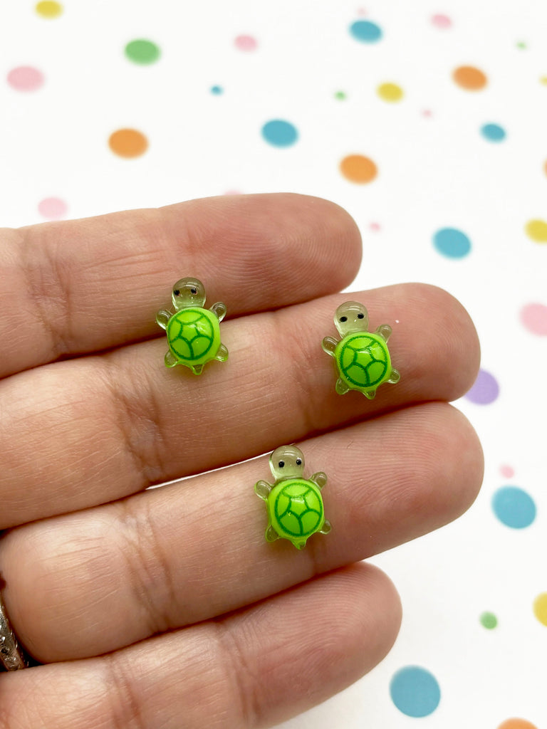 a person's hand holding a pair of tiny turtle earrings