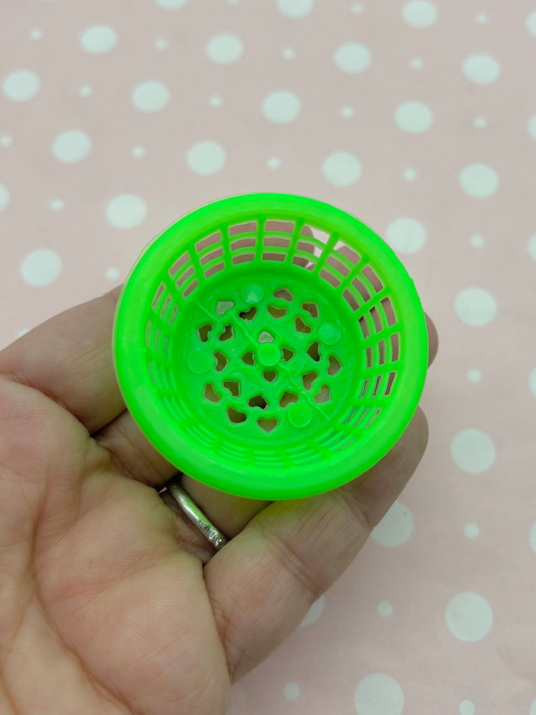 A hand is holding a small green plastic basket with a grid pattern on the inside.