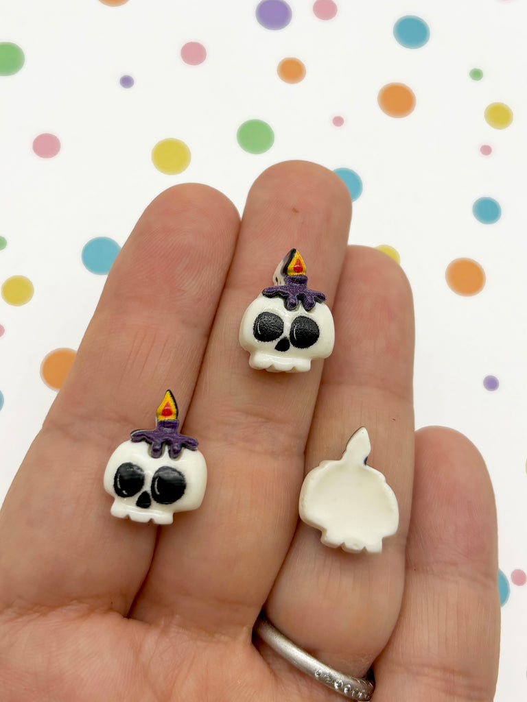 a hand holding a pair of skull earrings