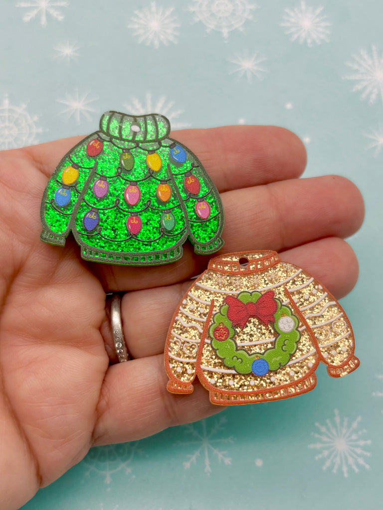 A hand holding two Christmas-themed ornaments, one green and one brown, against a snowy background.