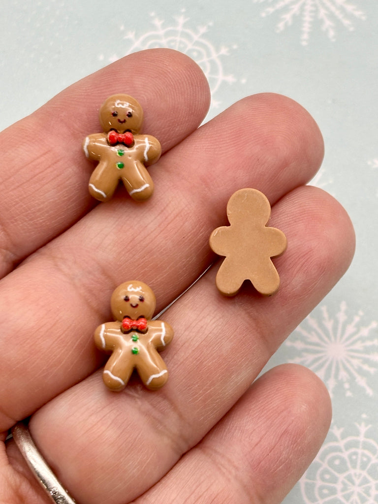 A hand holding three small gingerbread man figurines against a snowy background.