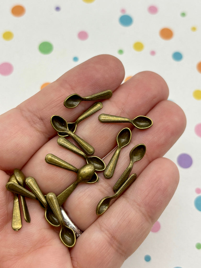 A hand holding a collection of small, brass-colored metal spoons against a background with colorful polka dots.