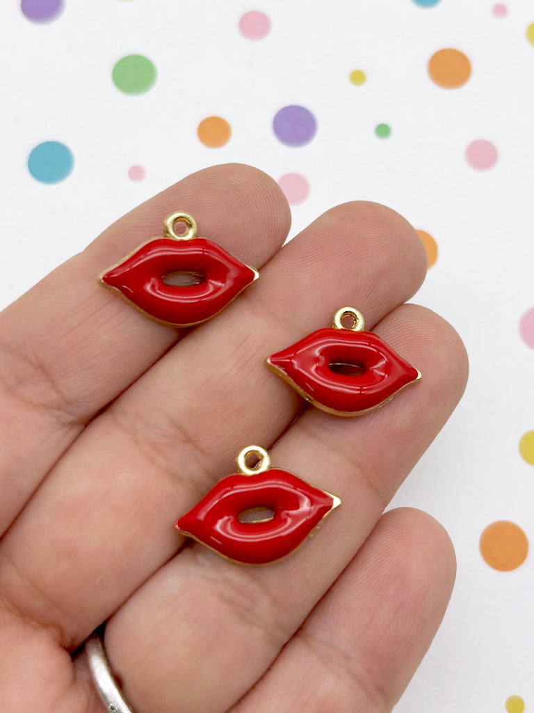 A hand holding three red enamel charms shaped like lips against a background with colorful polka dots.
