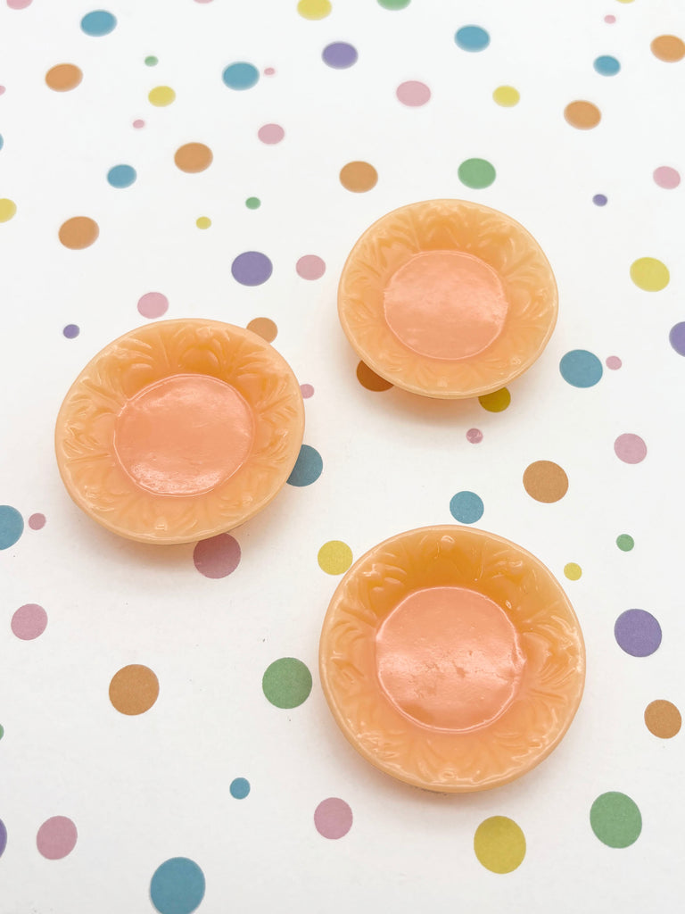 three small, round, orange-colored objects arranged on a white background with colorful polka dots.