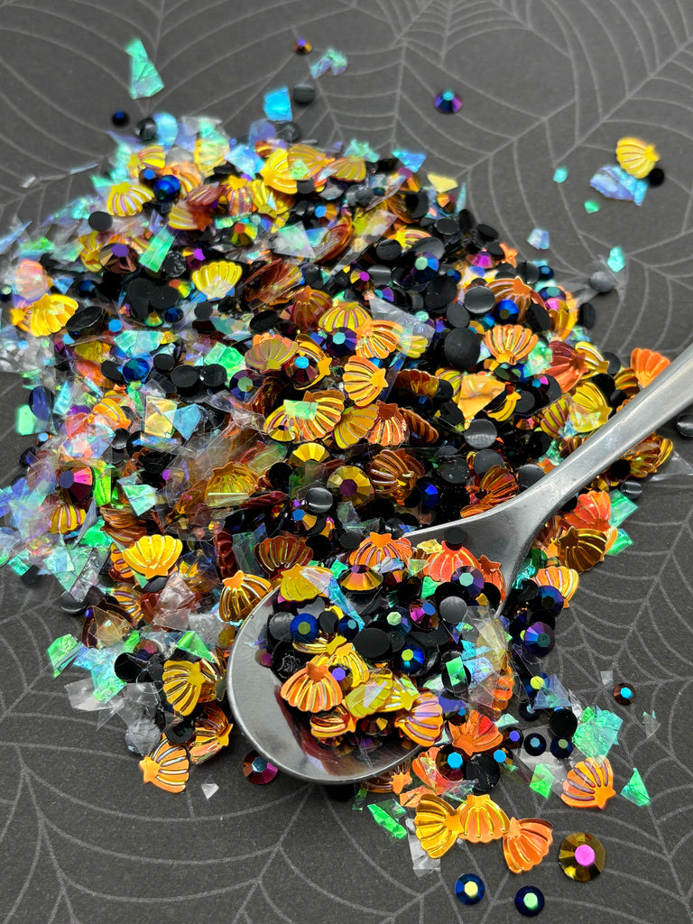 a pile of colorful beads, including seashells and glitter, scattered on a surface. A spoon is visible, with some of the beads spilling out onto the surface.
