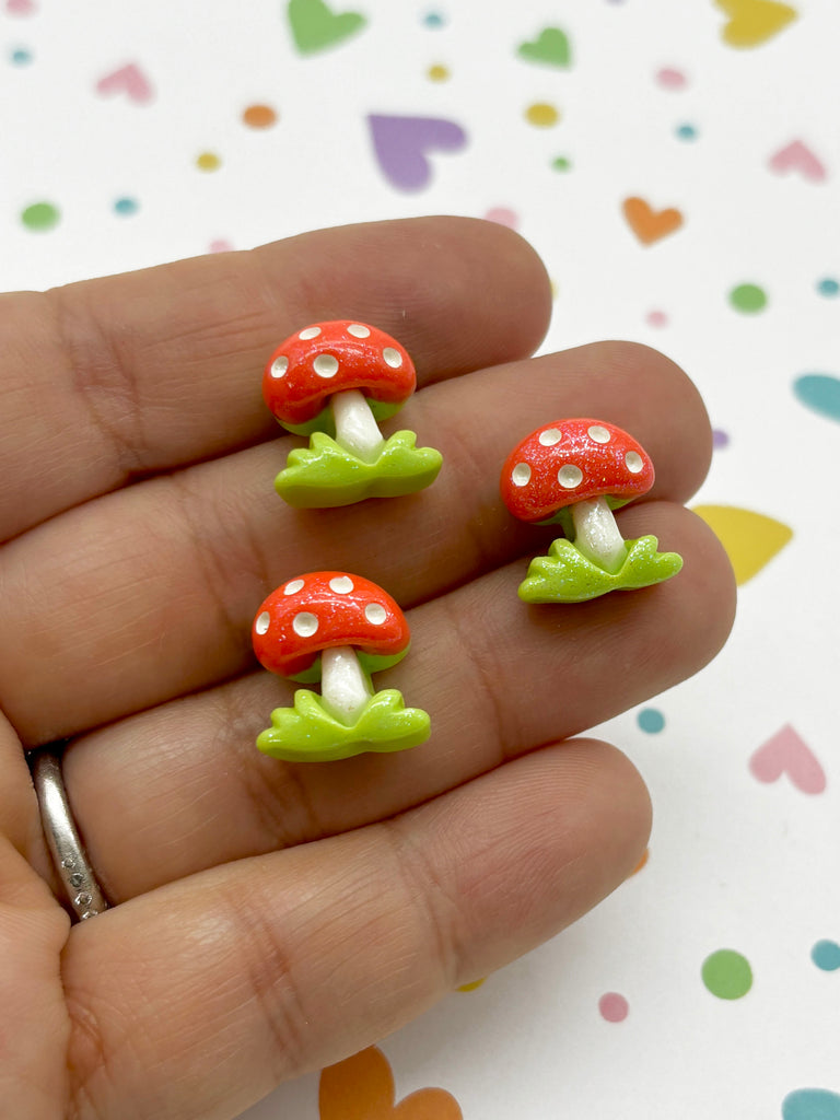 a hand holding three tiny red and green mushrooms