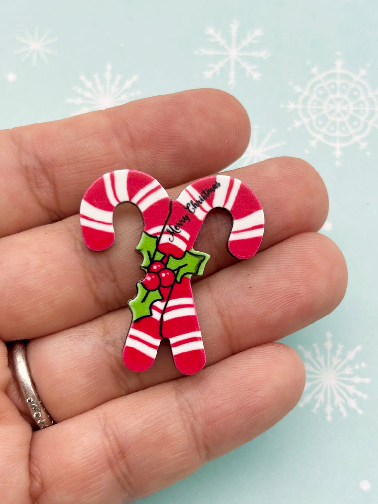A hand holding a small red and white candy cane pin with the text "Merry Christmas" written on it.