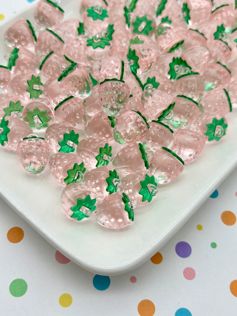 a white plate filled with numerous small, clear plastic beads that are shaped like strawberries. The beads are arranged in a visually appealing manner, creating a playful and colorful display.