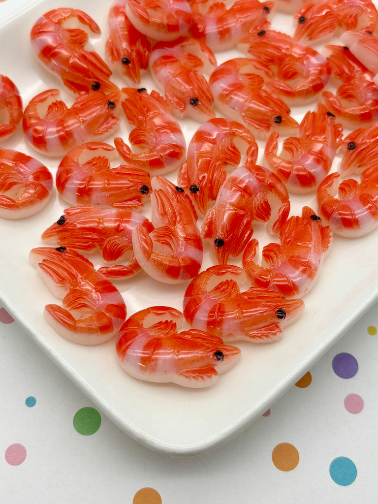 a white plate filled with numerous small, orange-colored plastic shrimp or crab-shaped objects. The shrimp appear to be made of a material that resembles plastic, giving them a shiny, artificial appearance. The plate is placed on a surface with colorful polka dots, adding a playful and vibrant touch to the scene.