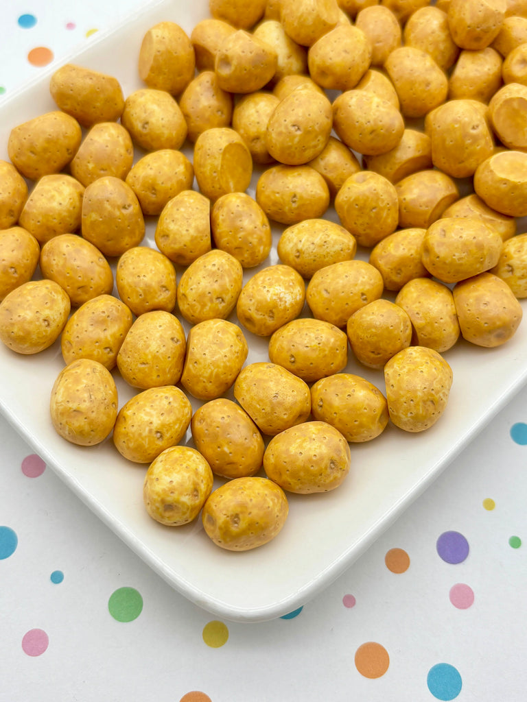 a white plate filled with small, round, yellow-colored snacks, possibly nuts or dried fruit, arranged in a visually appealing manner.