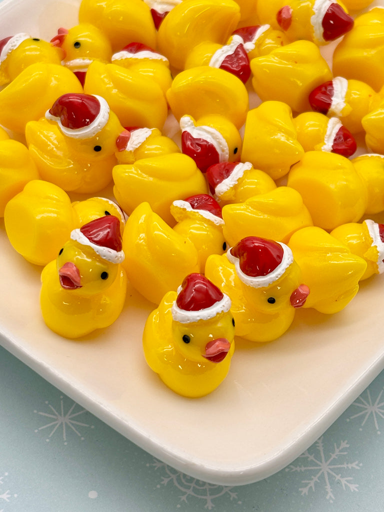 a white plate filled with yellow rubber duckies, each wearing a red Santa hat.