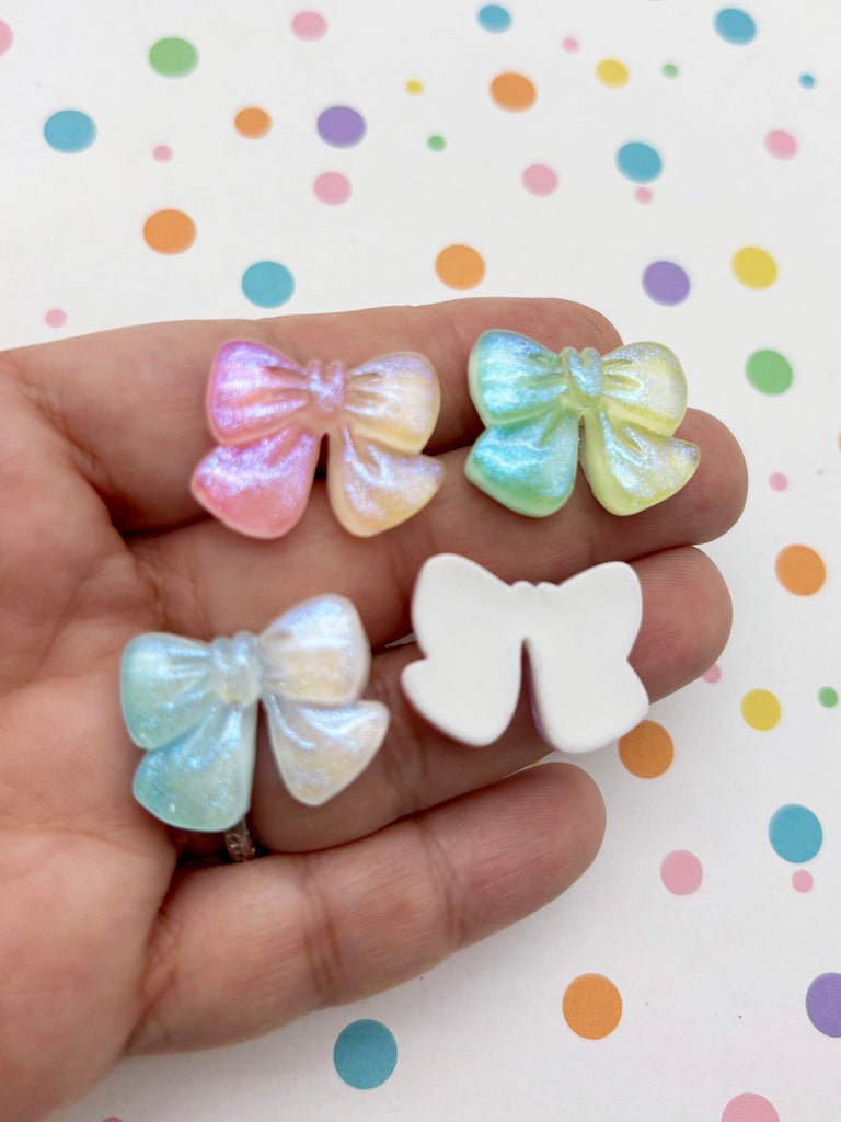 A hand holding four colorful, glittery bows against a background with polka dots.