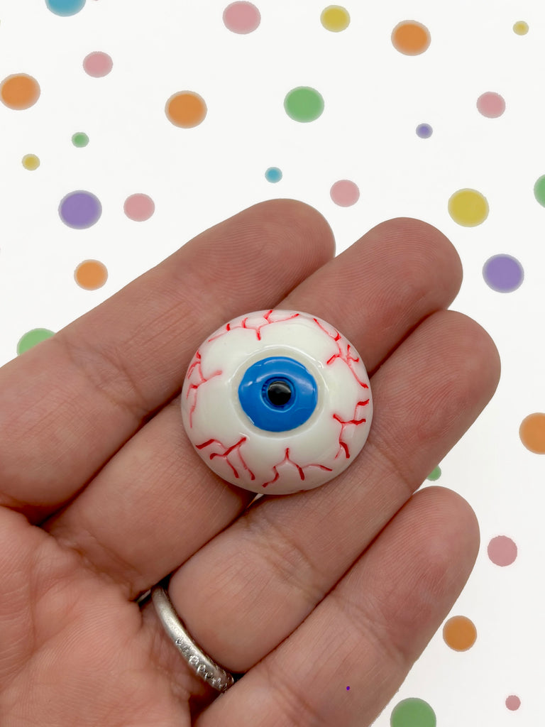 A hand holding a small, round object resembling an eye with red and blue accents against a background of colorful polka dots.