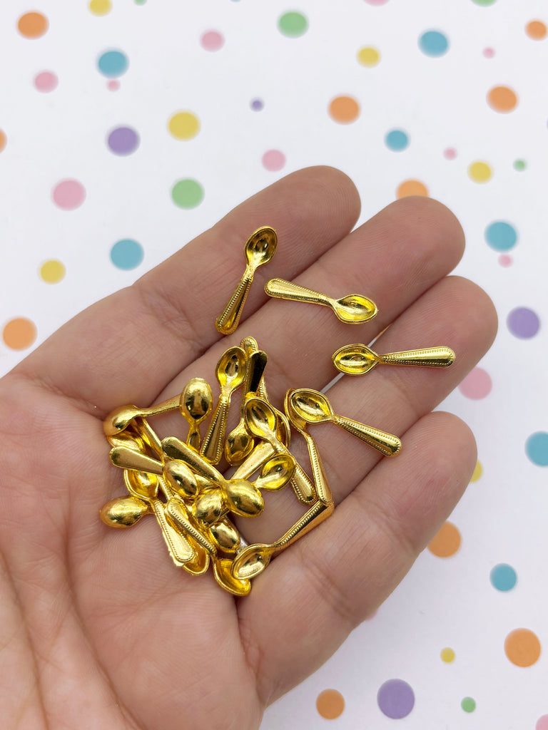 A hand holding a pile of small, shiny gold-colored spoons against a background with colorful polka dots.