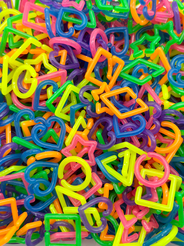The image is a colorful pile of various plastic shapes, including letters, numbers, and geometric forms, creating a vibrant and playful visual.