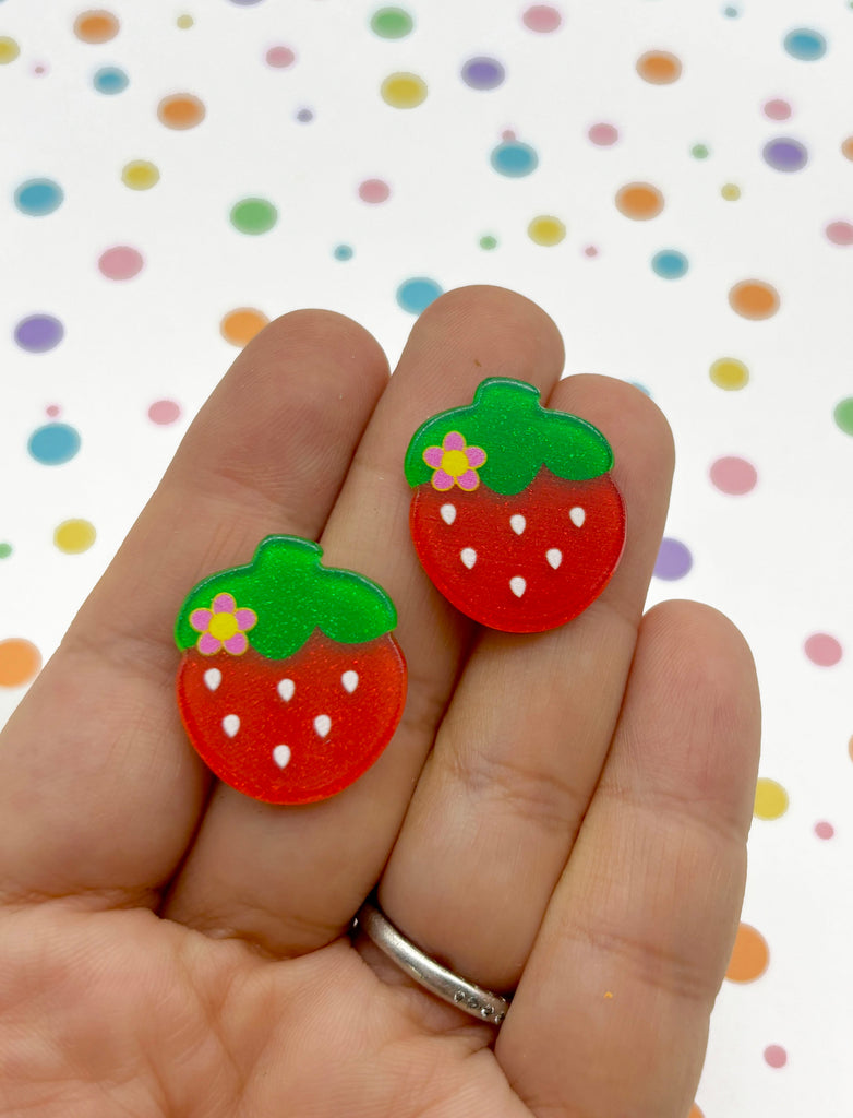 a hand holding a pair of red strawberry earrings