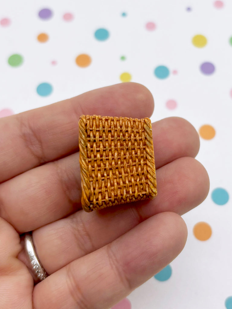 A hand holding a small, square-shaped object made of woven material against a background with colorful polka dots.