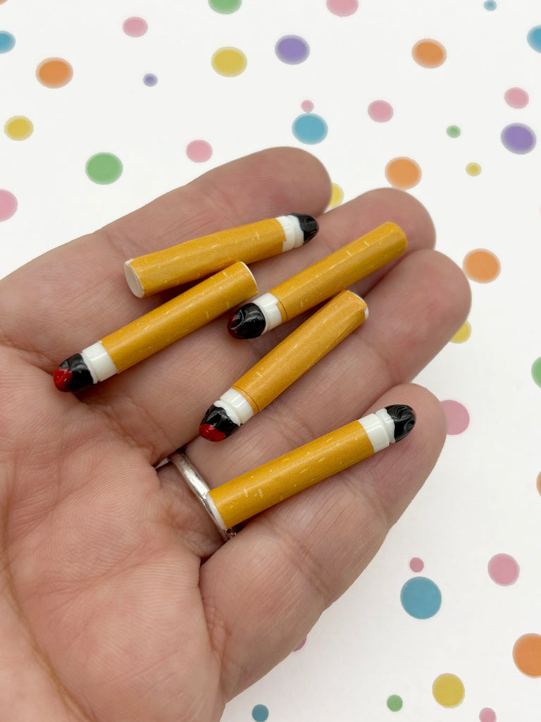 A hand holding several yellow pencils with black tips against a background with colorful polka dots.