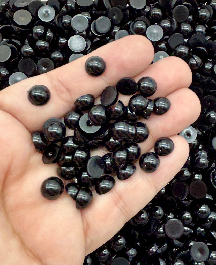 A hand holding a pile of black beads against a background of more black beads.