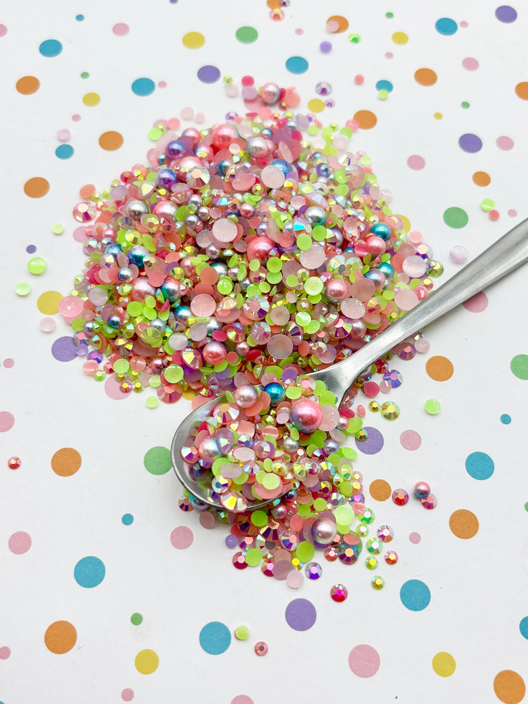 a pile of multicolored glitter beads on a white background, with a spoon partially submerged in the glitter.