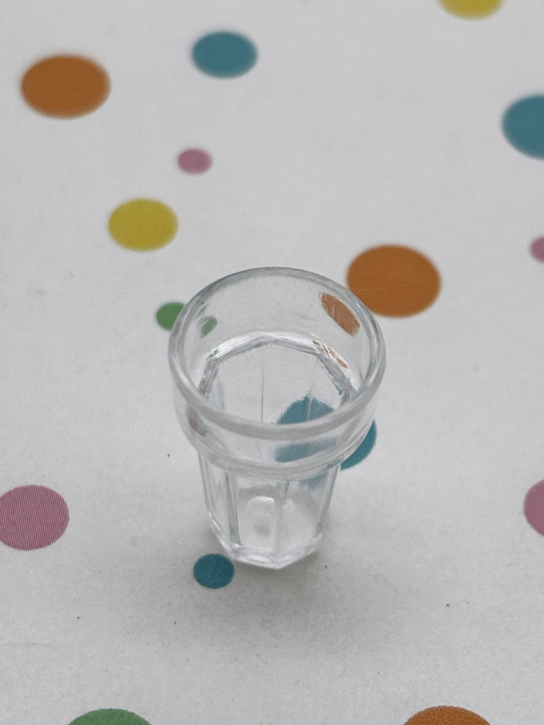 A clear glass cup sits on a white surface with colorful polka dots.