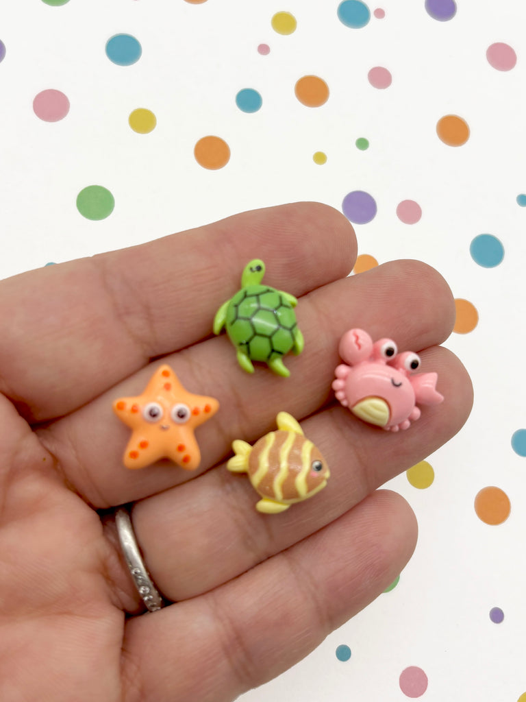 A hand holding a collection of colorful sea animal figurines against a background with polka dots.