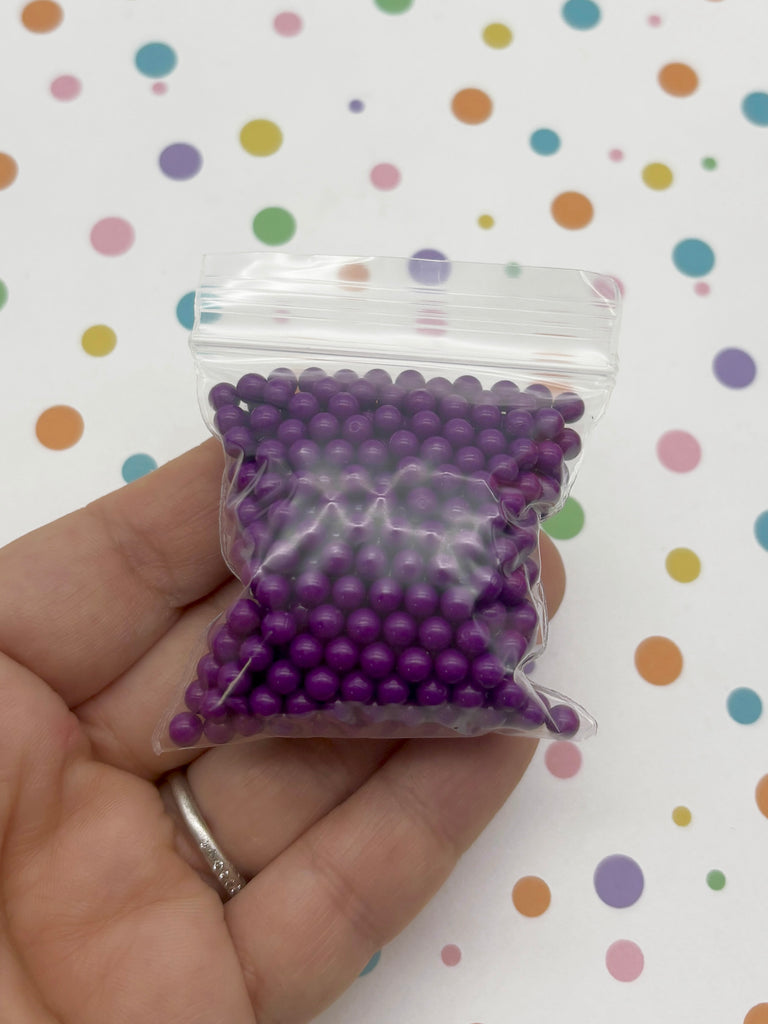 a hand holding a bag of purple beads