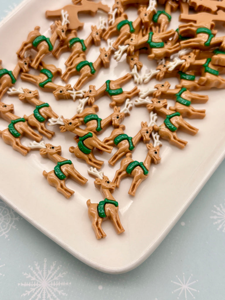 a white plate with a collection of brown toy reindeer wearing green scarves.