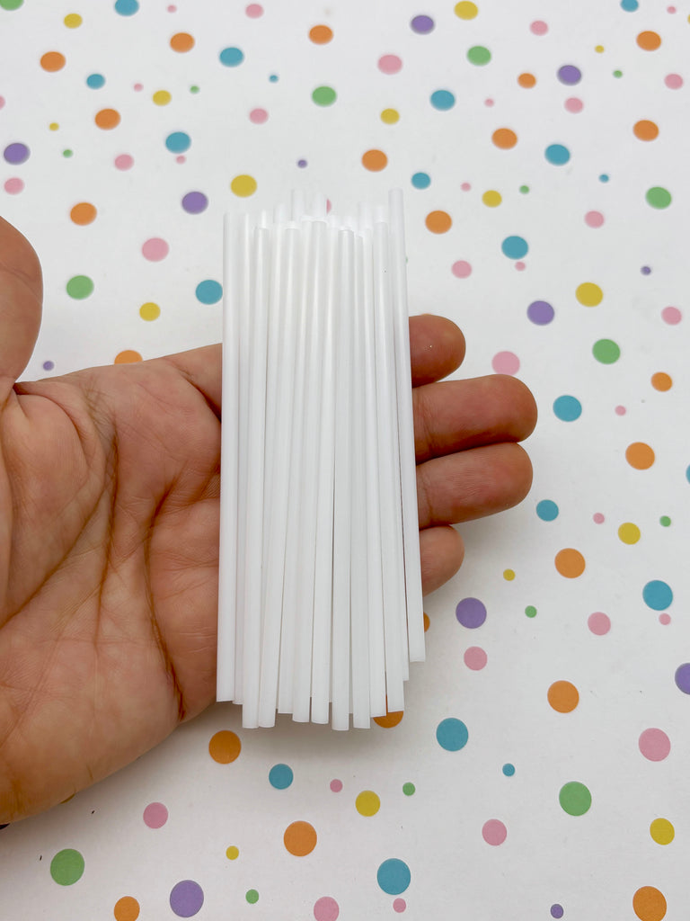 A hand holding a bunch of white straws against a background with colorful polka dots.