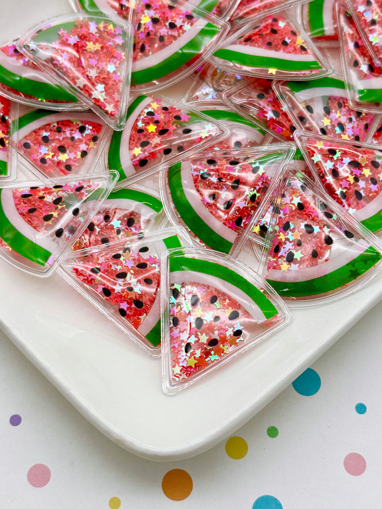 a white plate with a collection of watermelon-shaped objects, each with a green stripe and glittery stars. The objects are arranged in a visually appealing manner, creating a vibrant and playful display.