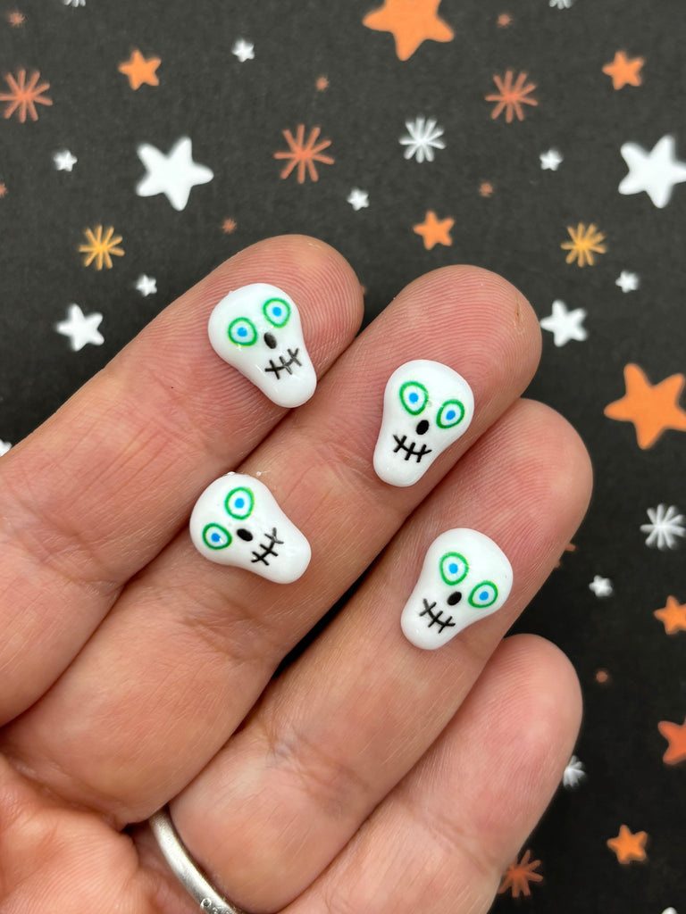 a hand holding a white and green skull shaped nail