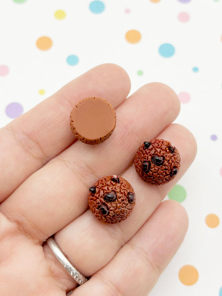 A hand holding two chocolate chip cookies against a background with colorful polka dots.
