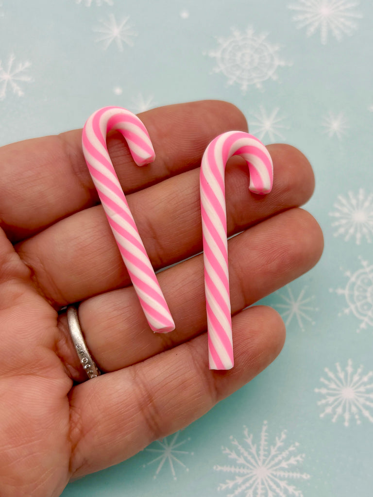 A hand holding two pink and white striped candy canes against a background of snowflakes.