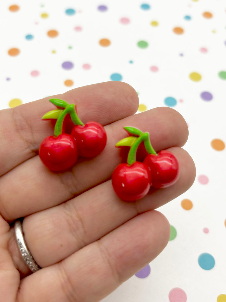 a hand holding a pair of tiny cherries