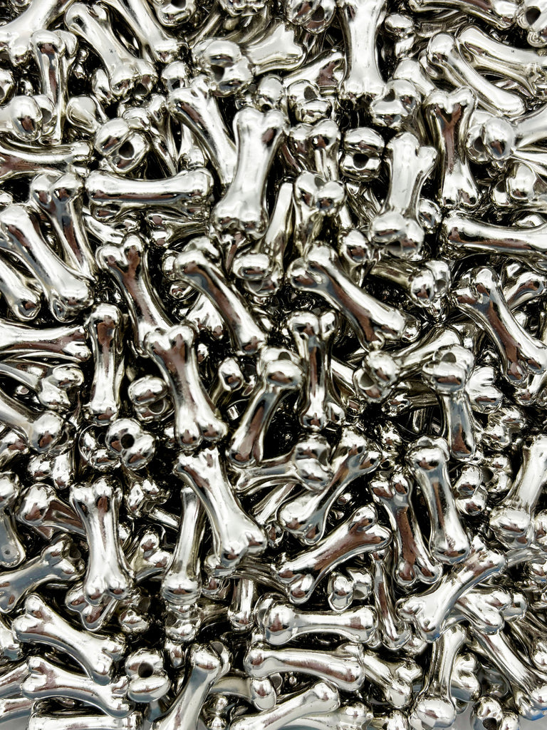 The image is a close-up of numerous silver-colored metal bones piled together, creating a visually striking and metallic texture.