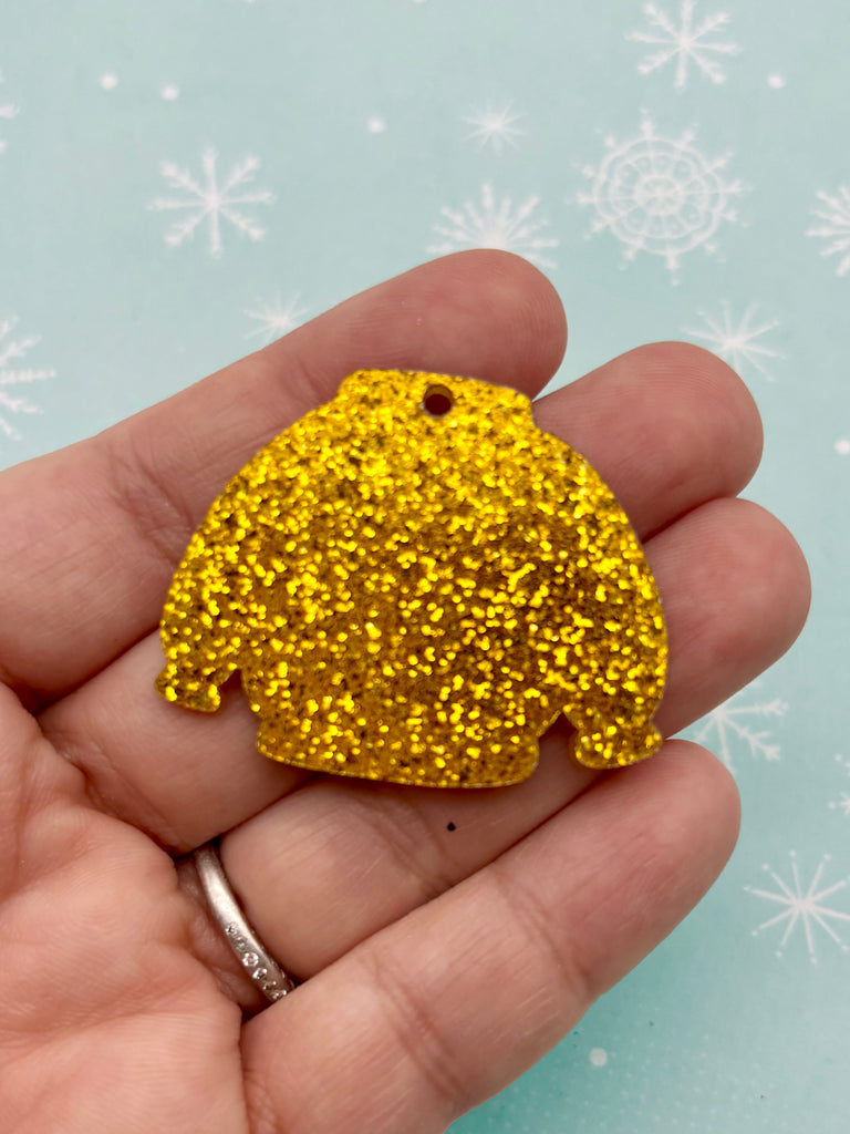 A hand holding a glittery gold-colored object resembling a sweater or a similar garment against a background with snowflakes.
