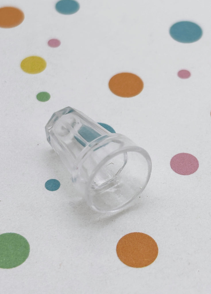 a clear plastic object, possibly a cup or container, placed on a white surface with colorful polka dots scattered around it.