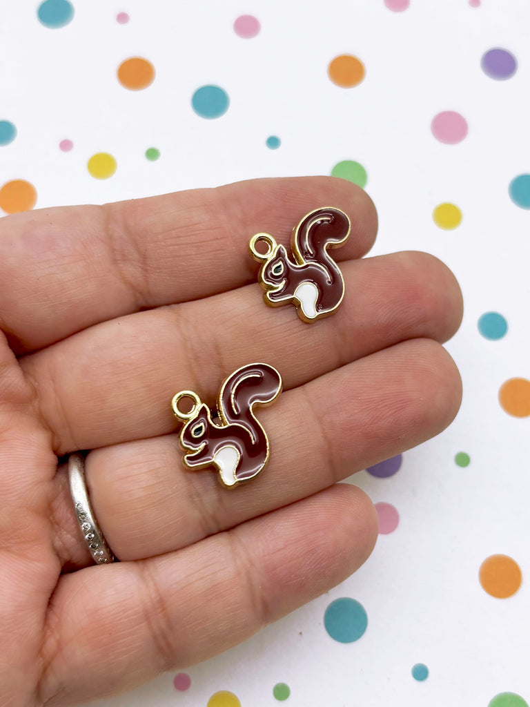 A hand holding two small, colorful squirrel charms against a background with polka dots.