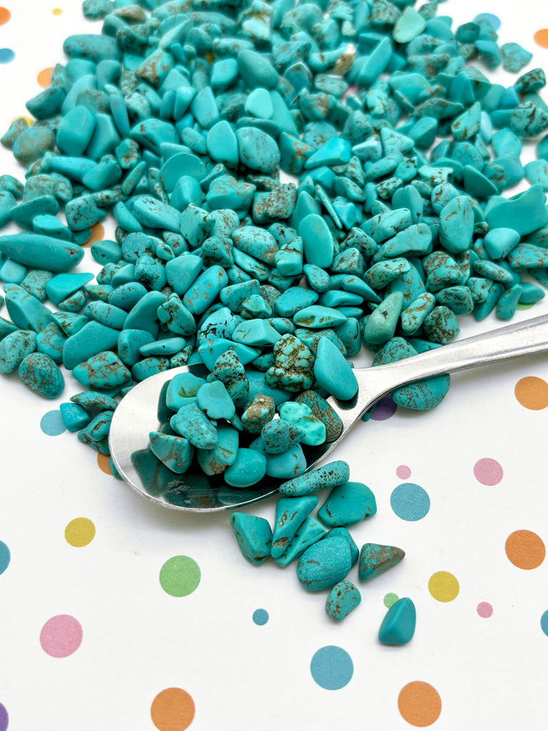 a spoon full of turquoise colored rocks and pebbles