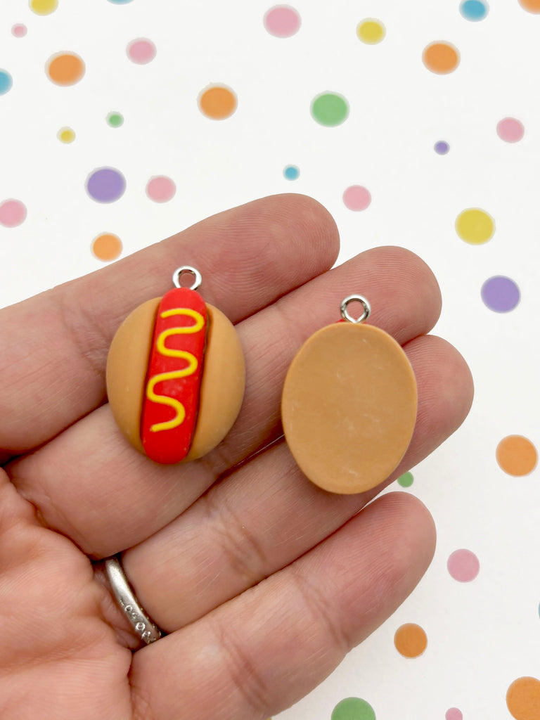 A hand holding two small, round charms shaped like hot dogs.
