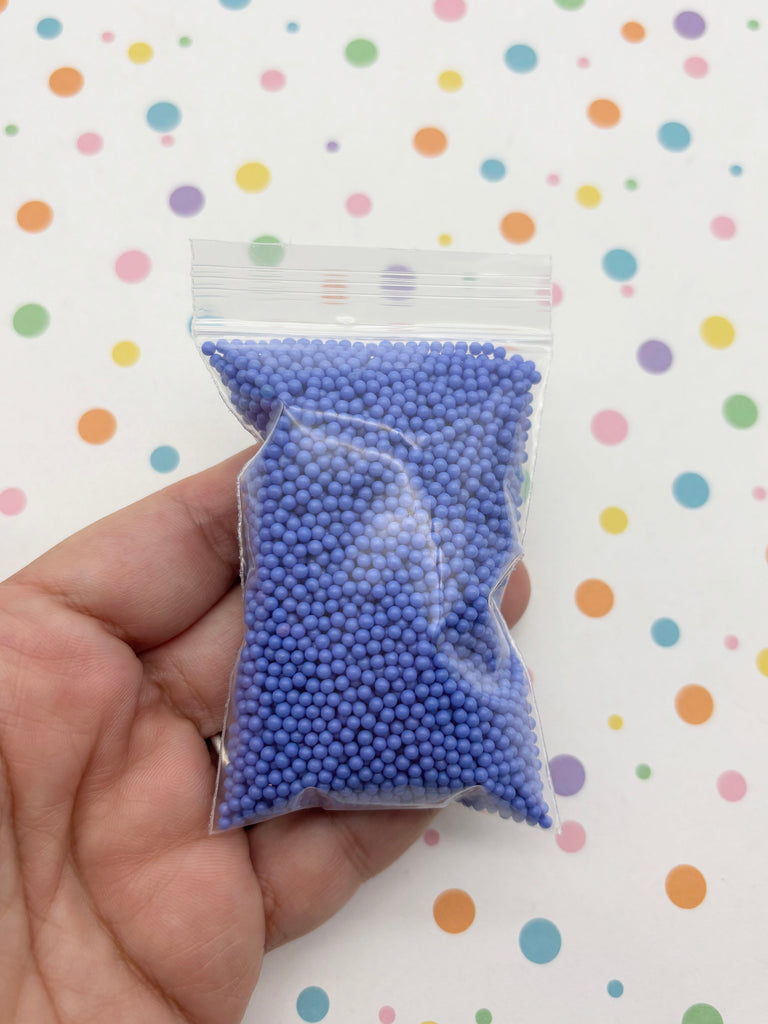 A hand is holding a small bag filled with purple beads against a background with colorful polka dots.